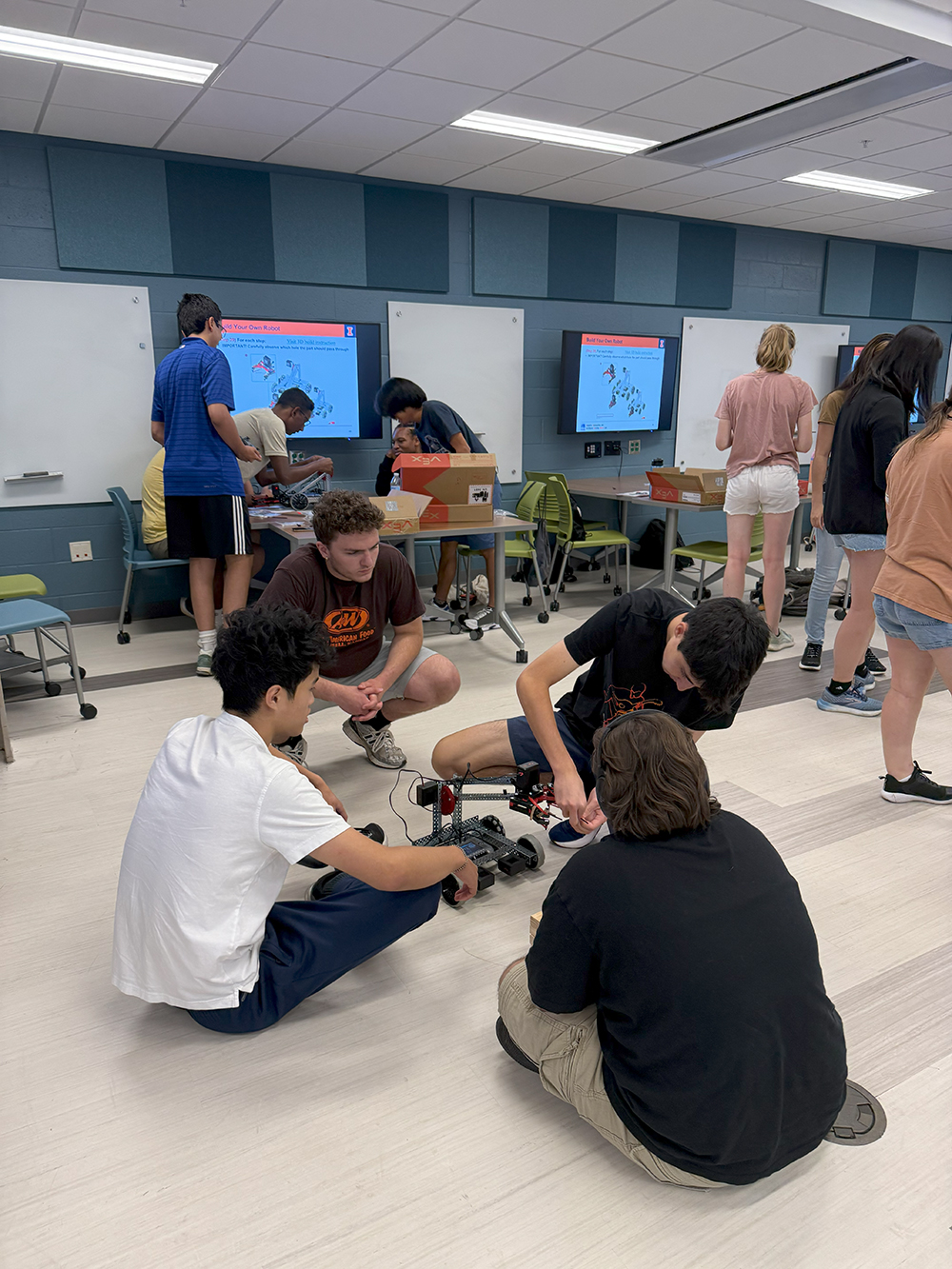 Students sitting on the floor of a classroom making adjustments to their robotics kits.