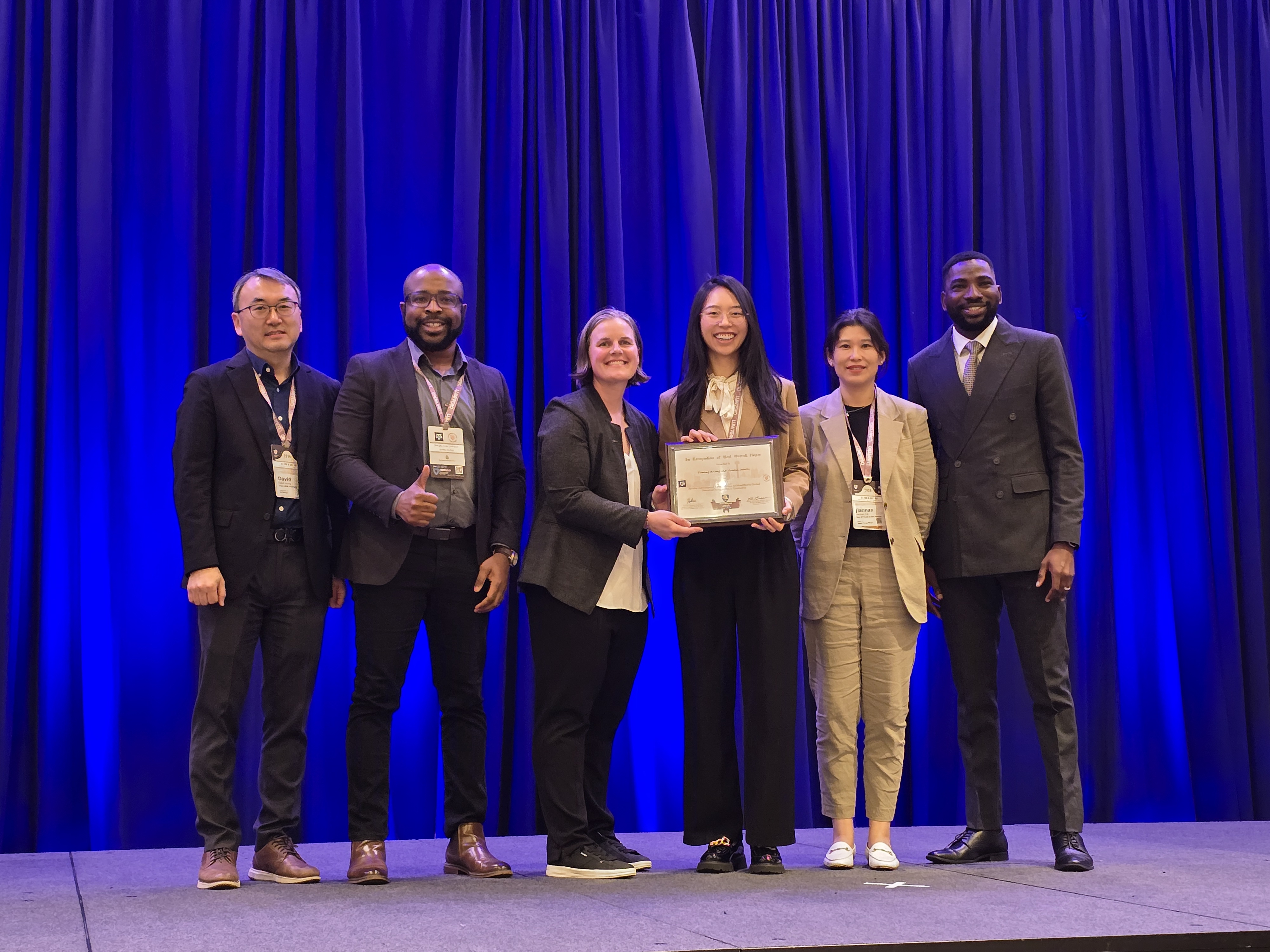 A group of people stand onstage as one accepts and award.