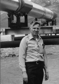 Professor Emeritus William J. Hall posing before the Alaska Pipeline, one of the projects on which he worked.