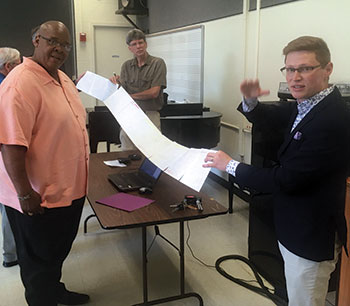 Dominic DiOrio, right, explains his composing process and displays the notes he made in planning the sequence of the sesquicentennial composition. Librettist Richard Powers, center, holds the other end of the paper. Performer Todd Payne is in the foreground at left.