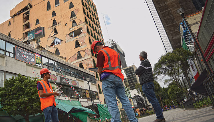 Hoskere, left, sends out a drone to automatically survey the facade of a heavily damaged building in Mexico City, while Neal, center, notes down details for a rapid visual assessment report under the supervision of Prof. Manuel Ruiz-Sandoval, right. The drone is visible over Nealâ€™s right shoulder.