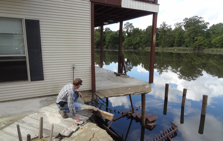 Stark surveys undermined house, missing earth retention structure and dock (see 3 piles from structure, sticking up), submerged steps to upper balcony and hanging fence.