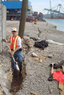 Olson uses a hand auger to take soil samples at the wharf in Port-au-Prince.  A toppled loading crane is visible in the background.
