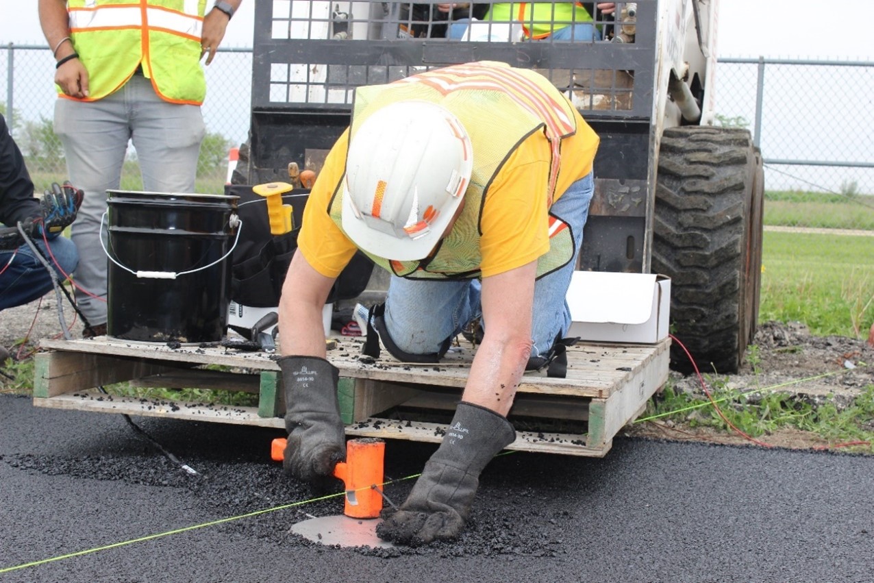 Imad Al-Qadi, ICT director and CEE Grainger Distinguished Chair in Engineering, places one of 12 pressure cells on a hot-mix asphalt mat at 290 degrees Fahrenheit before compaction on May 15. The pressure cells will measure pressure at the bottom of the stone-matrix asphalt layer while testing. This is the first time pressure cells are installed at a high temperature during layer compaction, according to Al-Qadi, who tried the technique for the first time while instrumenting the Cagliari Airport in Italy.